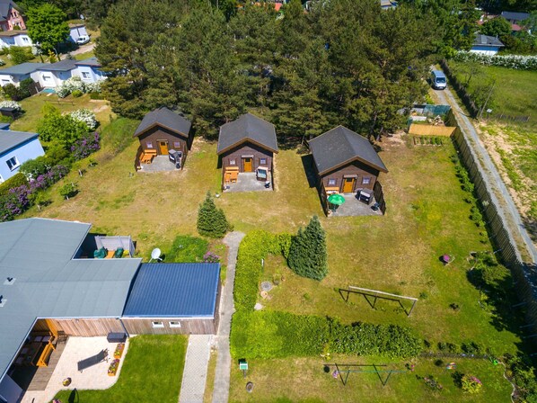 Vue aérienne d’un quartier résidentiel avec trois maisons en bois, chacune dotée d’un porche et d’un petit jardin.