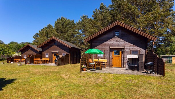 A row of wooden cabins with outdoor seating and a barbecue area. - Blockbohlenferienhaus Braun - Blockhaus (Koserow)
