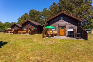 Une rangée de cabanes en bois, dotées d’un espace extérieur avec des sièges et d’un coin barbecue.