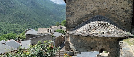 A stone building with a sloped roof, surrounded by lush green mountains and a clear sky.