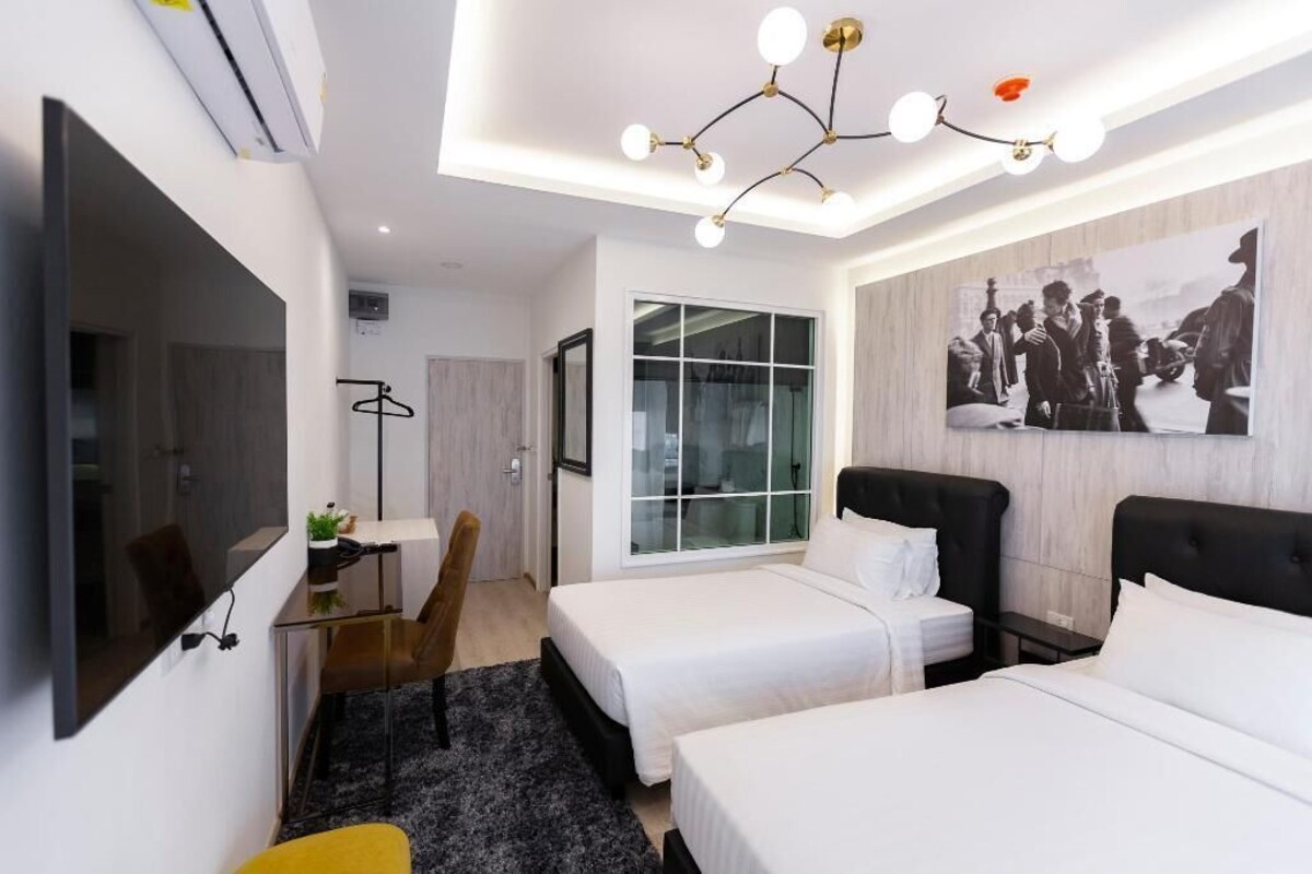 A hotel room with two beds, a desk, a chair, a large window, and a ceiling light fixture.