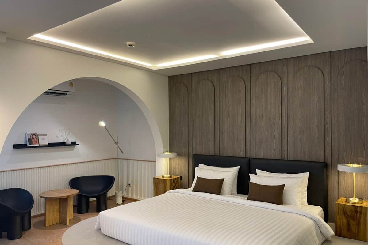 Une chambre moderne avec un grand lit, une arche murale aux lignes courbes, un petit coin salon et un mur revêtu de panneaux en bois.