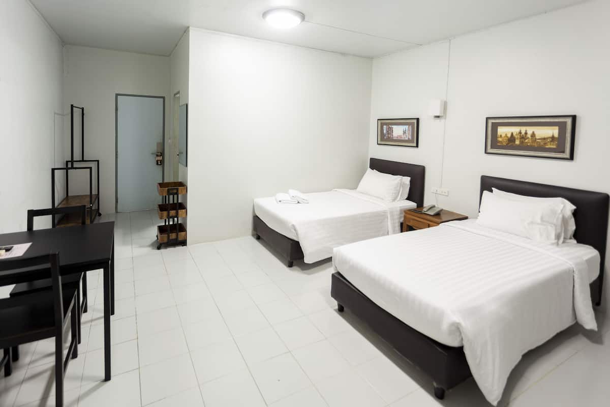 Une chambre d’hôtel avec deux lits, un bureau et une chaise. Des tableaux encadrés ornent le mur.