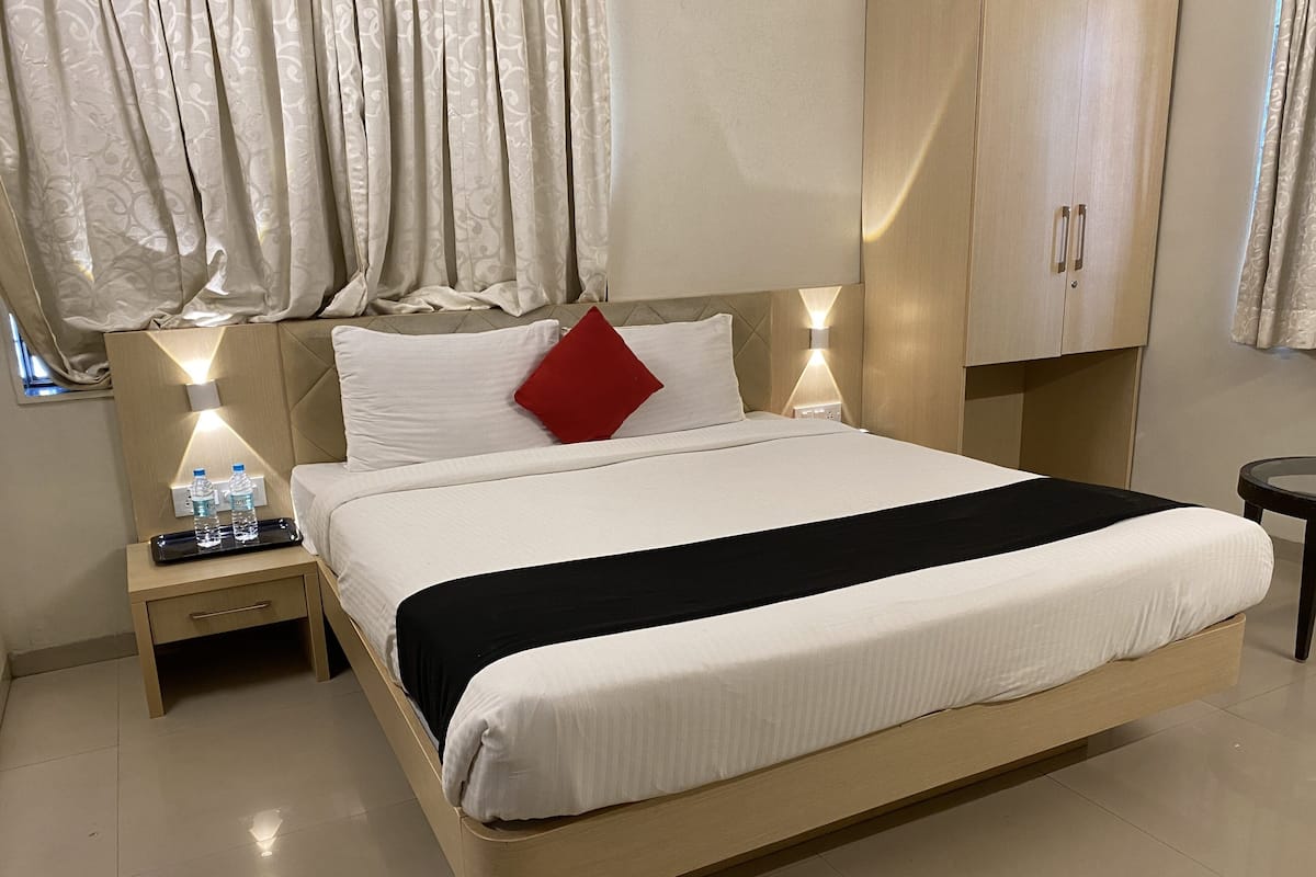 A hotel room with a large bed, a nightstand with a lamp, and a wardrobe.