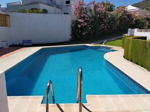 Una piscina rettangolare con superficie d'acqua cristallina e blu, circondata da un muro bianco e un siepe curata.