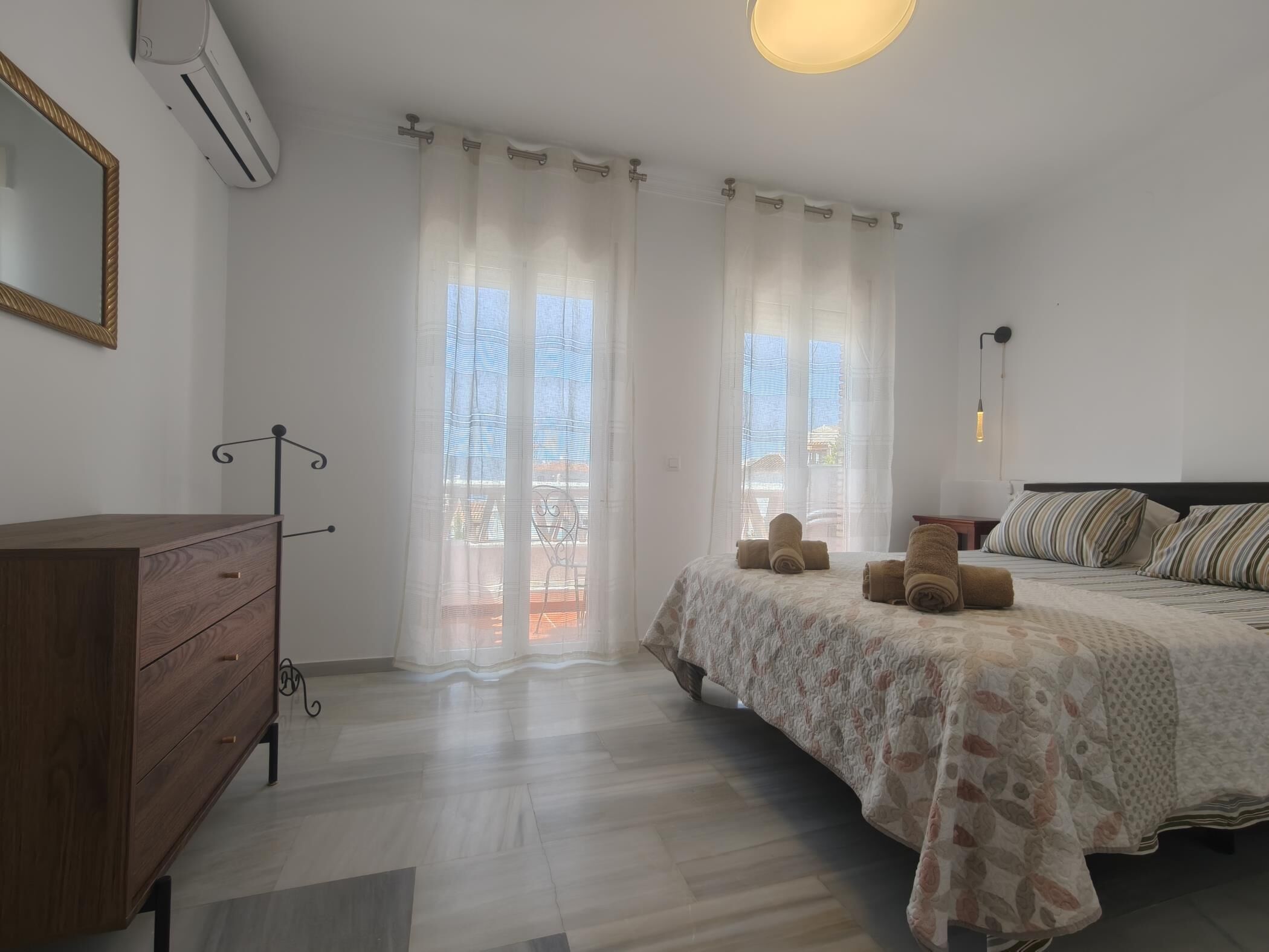 A bedroom with a bed, a wooden dresser, a mirror, and an air conditioning unit.