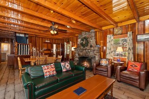 A log cabin interior with a stone fireplace, leather furniture, and wooden beams.