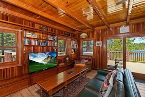 Un interior de madera con una televisión, estanterías, un sofá y vistas al exterior.