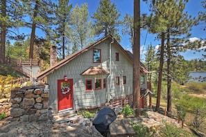 Una cabaña con base de piedra, puerta roja y terraza de madera.