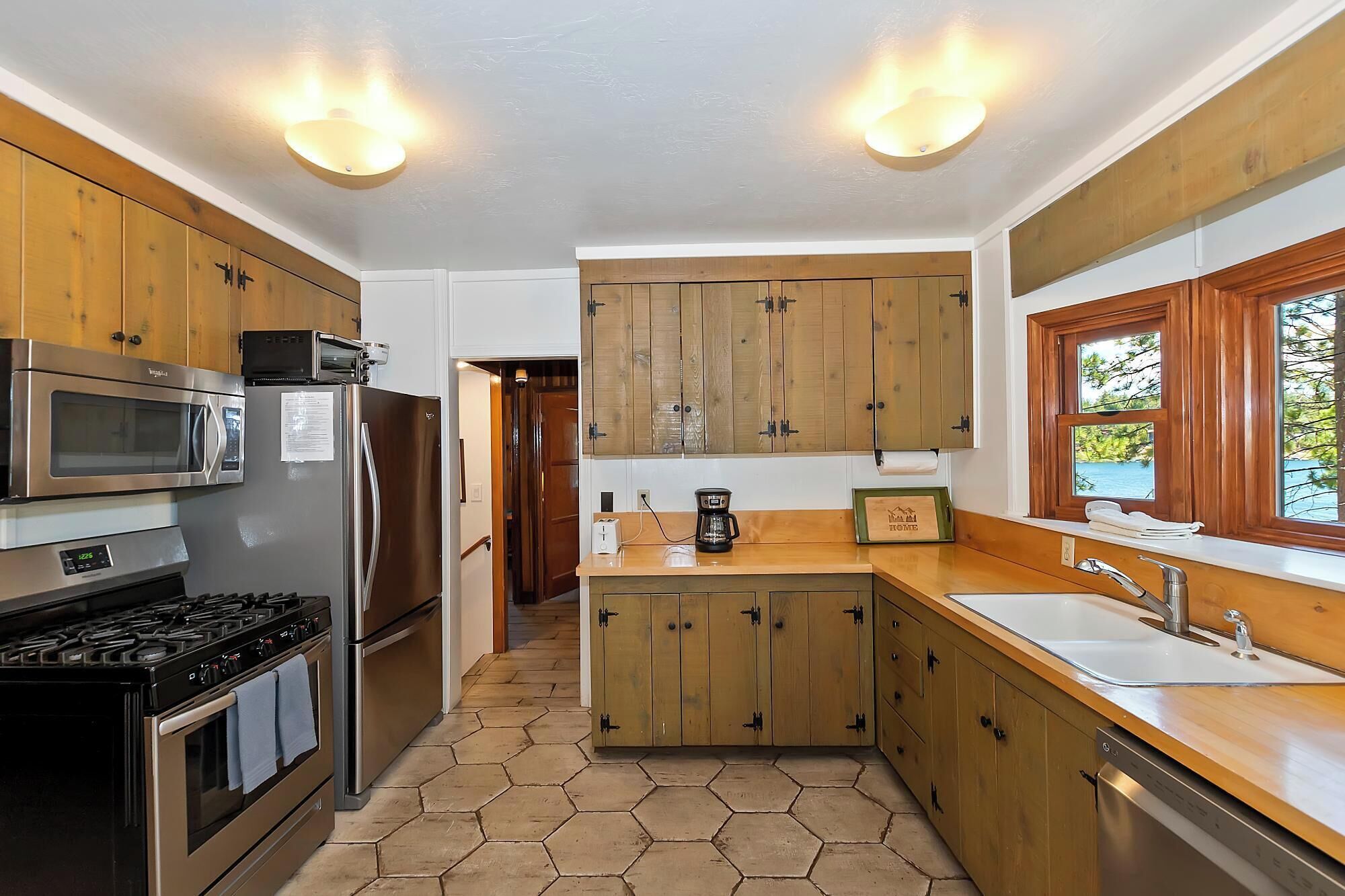 A kitchen with wooden cabinets, stainless steel appliances, a hexagonal tile floor, and a window with a view.