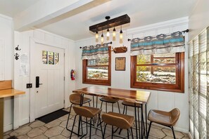 A kitchen with a wooden table, four stools, and two windows with curtains.