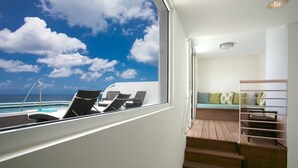 Un balcon avec vue sur l’océan, un coin salon avec des coussins et un escalier en bois.
