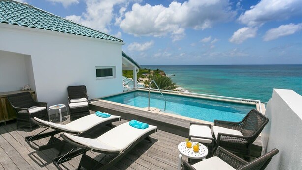 Un espace piscine aménagé sur le toit, avec des chaises longues et une table, offrant une vue imprenable sur une mer d’un bleu profond.