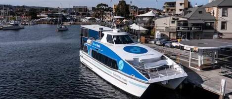 Un ferry moderno atracado en un puerto deportivo, con un paisaje urbano al fondo.