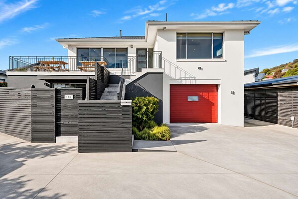 A modern two-story house with a red garage door, a staircase leading to the upper level, and a number '186' sign on the fence.
