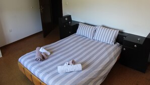Een net opgemaakt bed met gestreept beddengoed en kussens, twee nachtkastjes met lades, en een deur op de achtergrond.