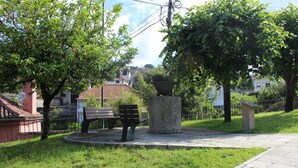 Een park met een ronde stenen bank, een grote plantenbak en een geplaveid pad.