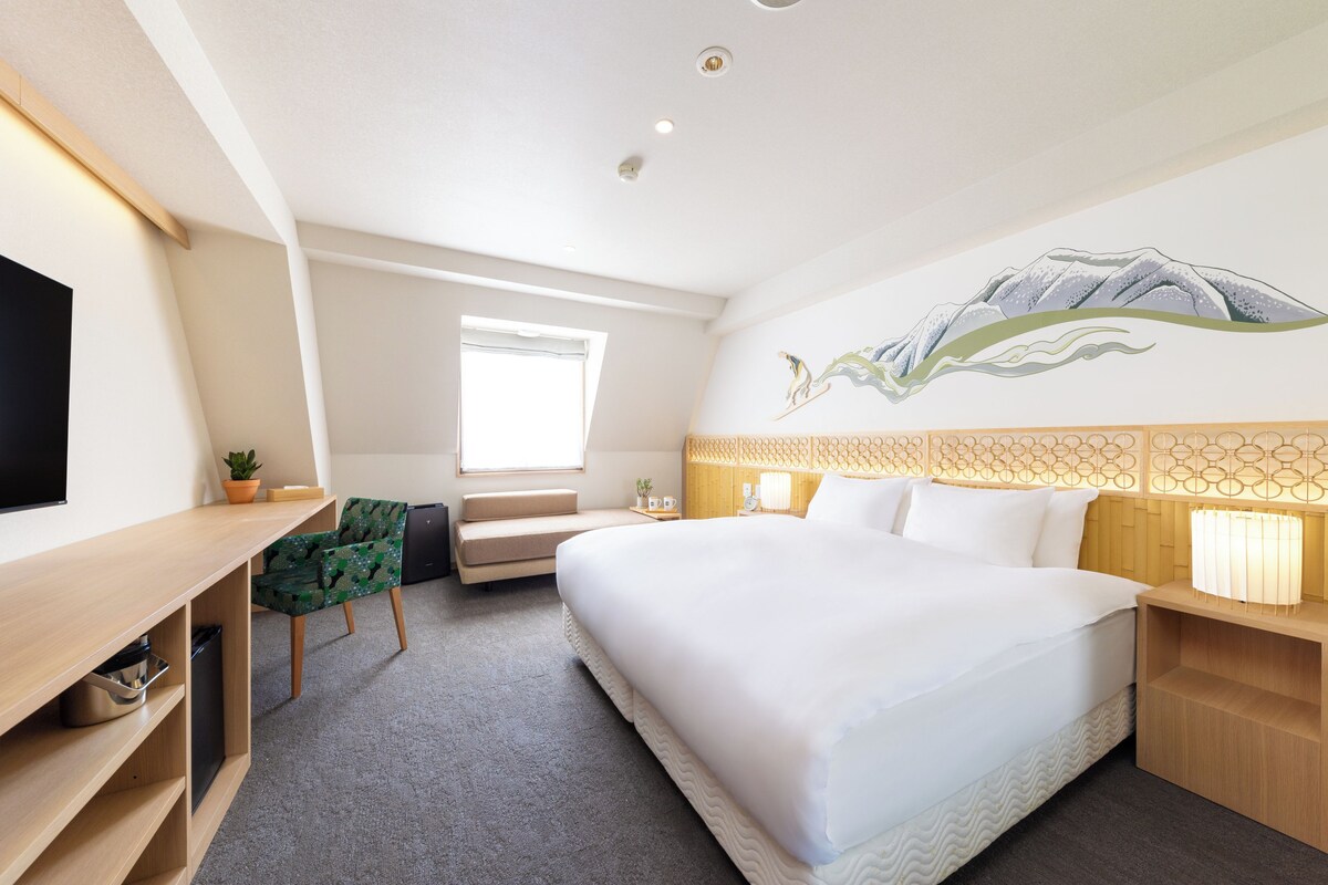 Une chambre d’hôtel équipée d’un lit, d’un bureau, d’une chaise, d’une télévision, d’une fenêtre et d’une décoration murale.