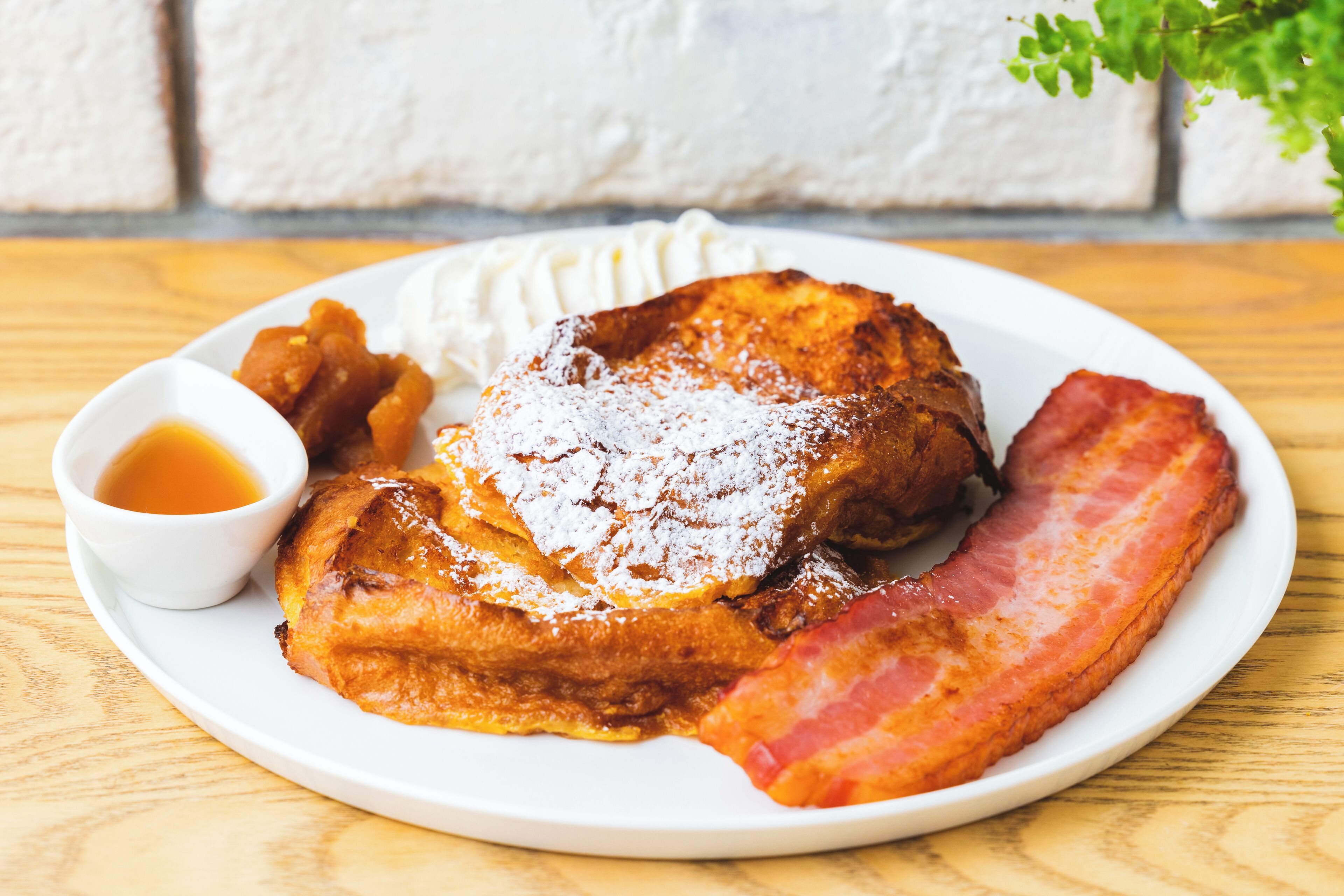 Une assiette avec un œuf au plat, des lardons, des pommes de terre rissolées et une petite tasse de sirop.