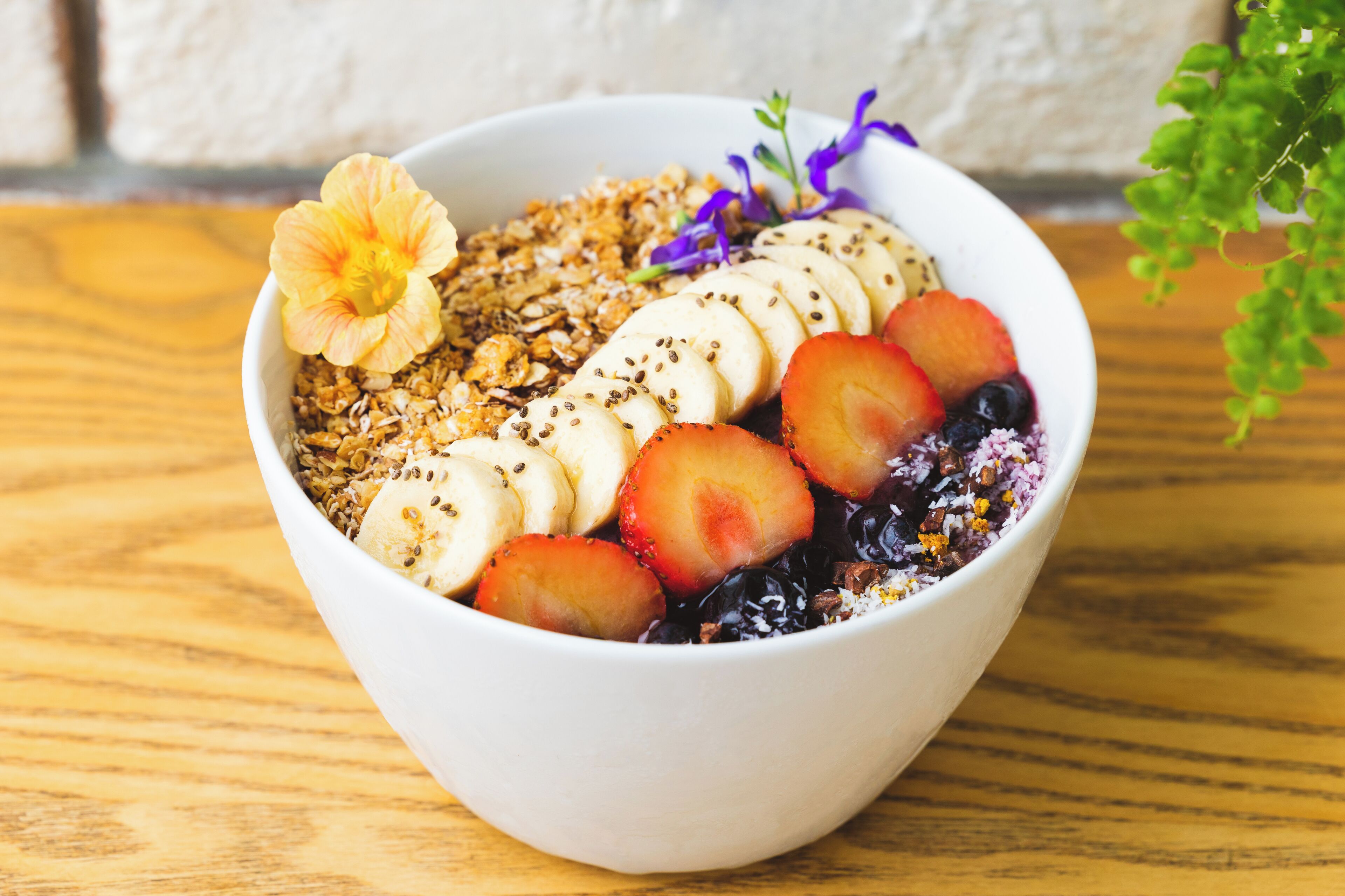 A bowl of fruit and granola on a wooden table.
