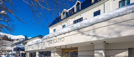 Un hotel con fachada cubierta de nieve, cielo azul despejado y entrada visible.