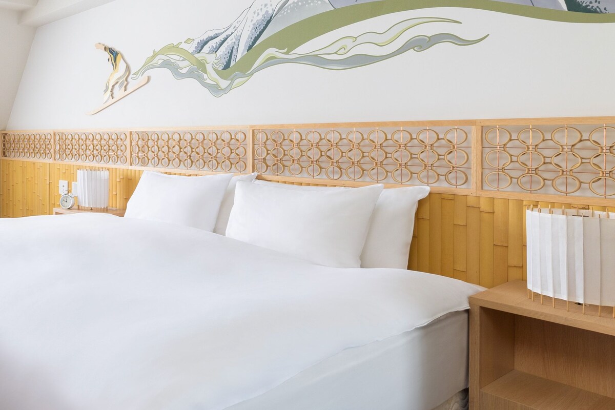 Une chambre d’hôtel avec un grand lit, une tête de lit en bois ornée d’un motif géométrique et une fresque murale.