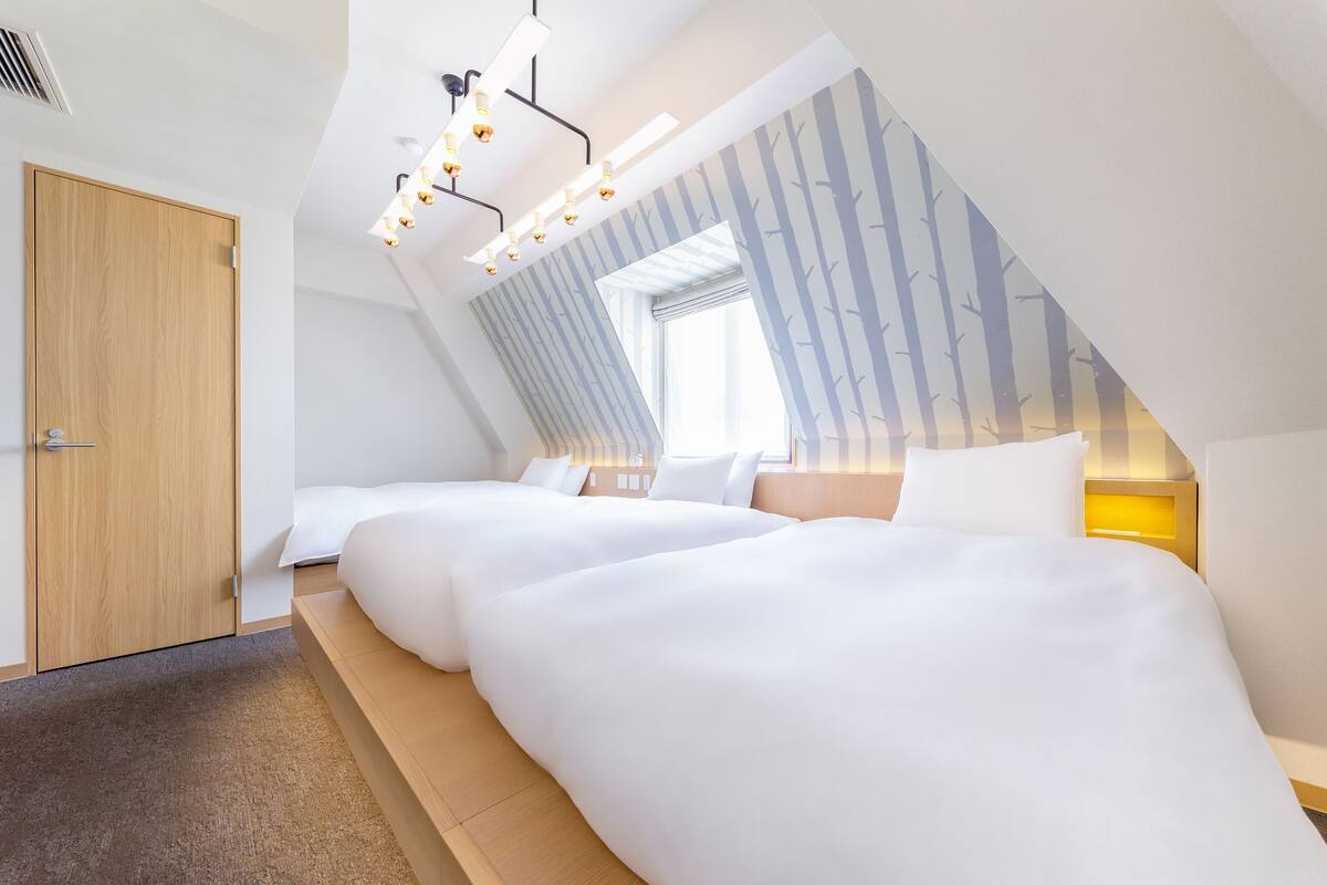 A modern bedroom with a sloped ceiling, a wooden door, and a large window.