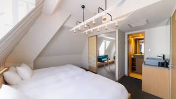 Una habitación de hotel moderna con una cama grande, un pequeño espacio de descanso, una kitchenette y vistas a la ciudad.