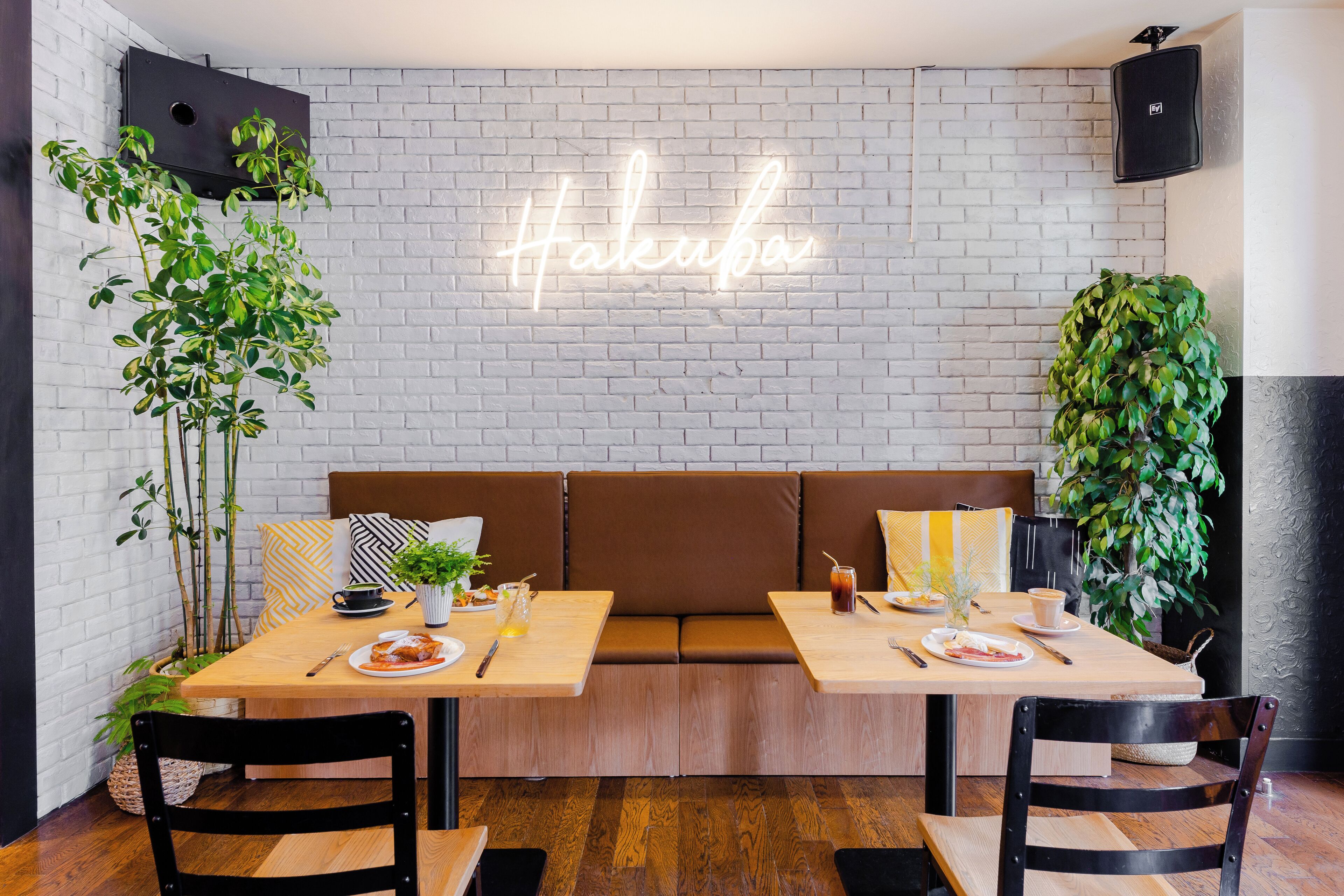 A modern cafe with a neon sign, wooden tables, and cushioned seating.