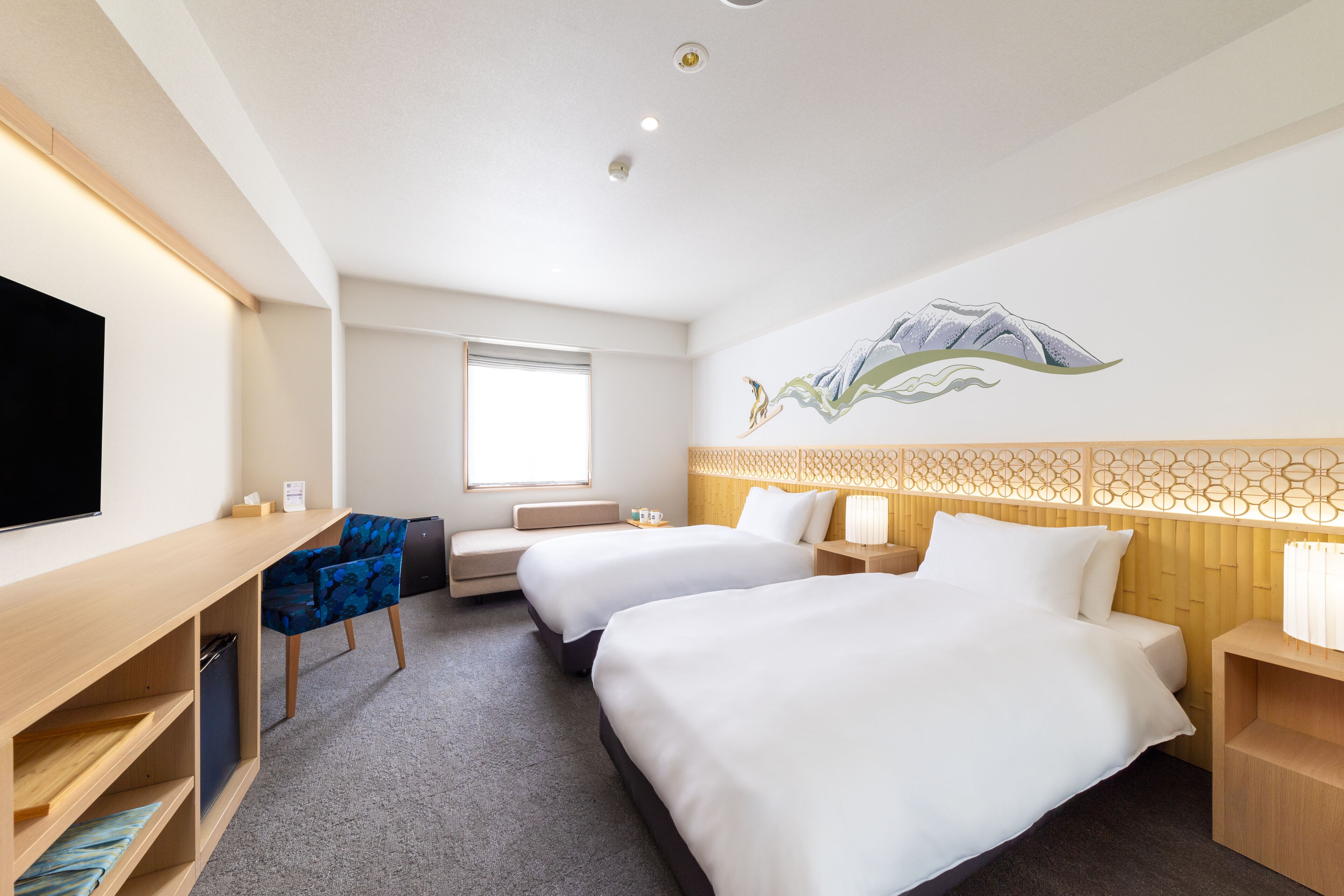 A hotel room with two beds, a desk with a chair, a TV, and a window.