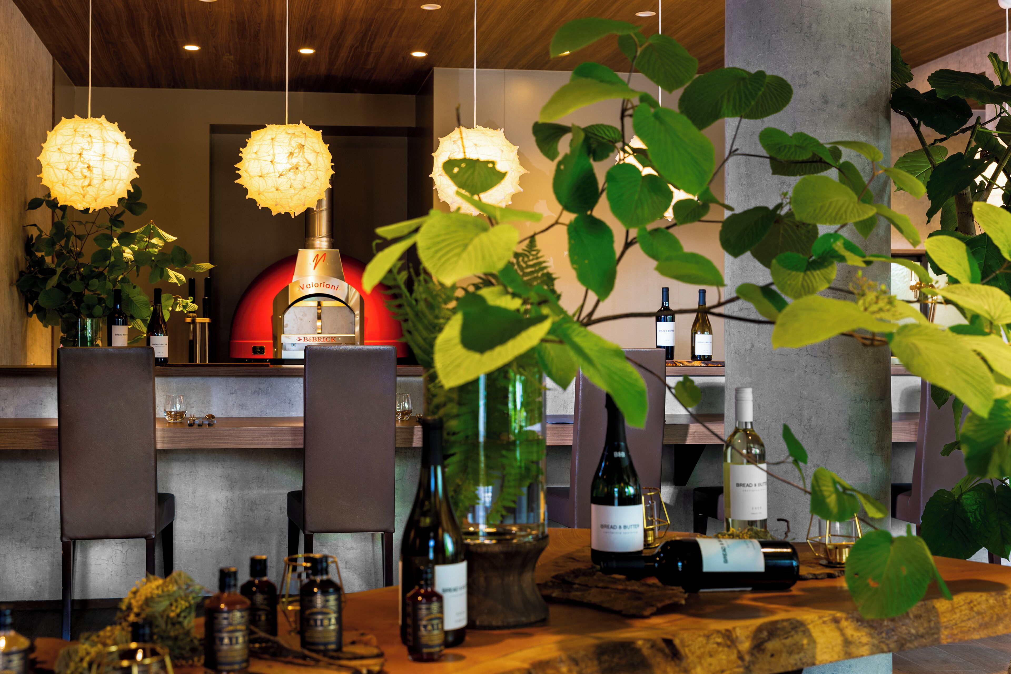 Un espace bar avec de nombreuses bouteilles de vin, une plante en pot et des luminaires suspendus.