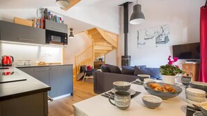 A modern kitchen with built-in appliances, a dining area with a white table, and a living room with a sofa and a TV. - Apartment Bailicimes, Morzine (Morzine)