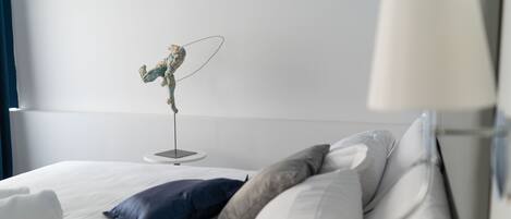 A modern hotel room with a bed, pillows, a standing fan, and a nightstand.