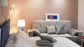 Une chambre à coucher moderne avec un lit, un canapé, une table de chevet, une lampe et un tableau encadré au mur.
