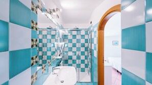 Un baño con azulejos blancos y azules formando un diseño de cuadros, un lavamanos blanco y un box de ducha de vidrio.