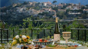 Una mesa con una botella de vino, cuencos y un ramo de flores, con vistas a un pueblo montañoso.