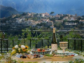 Una mesa con una botella de vino, cuencos y un ramo de flores, con vistas a un pueblo montañoso.