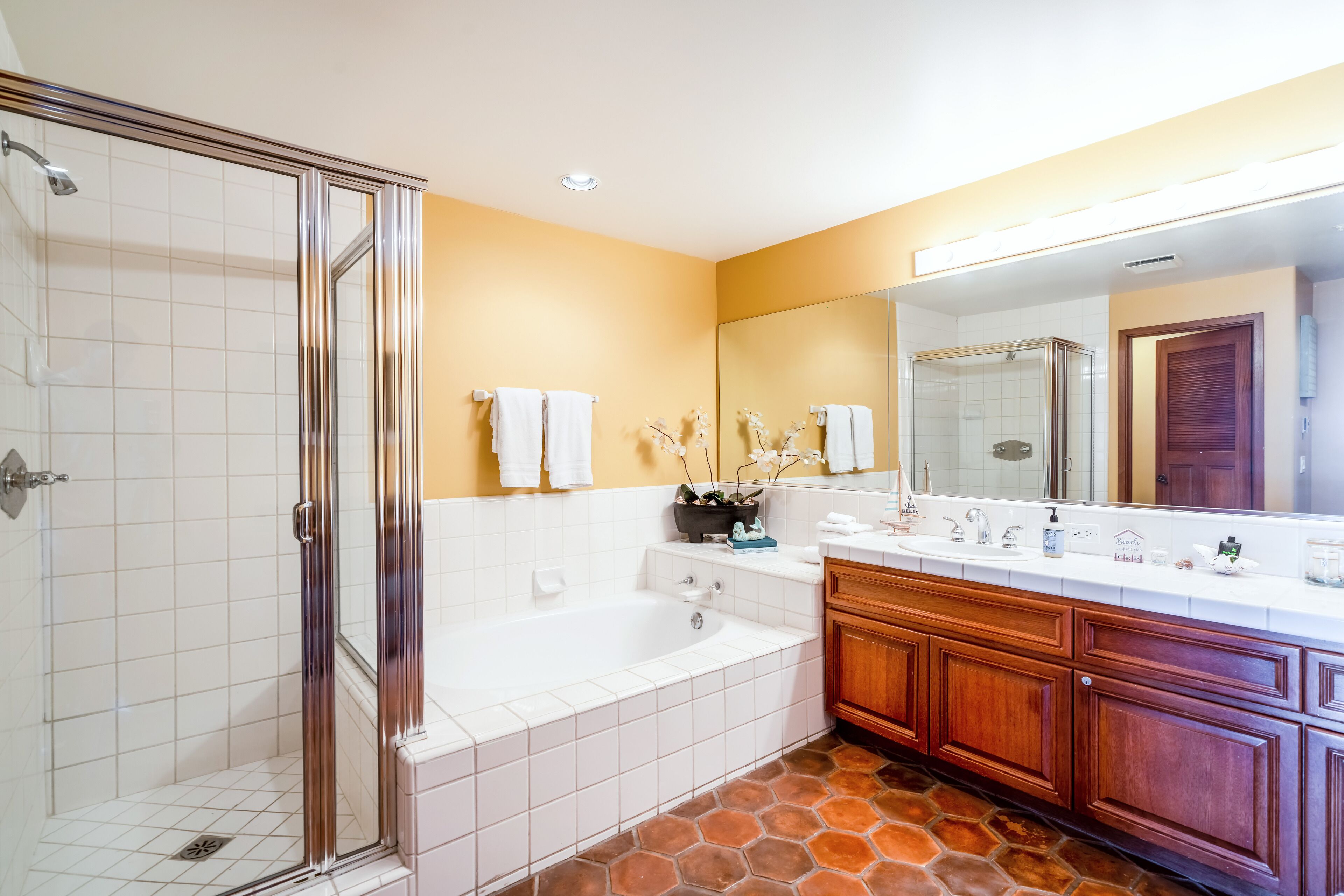 A bathroom with a glass shower enclosure, a bathtub, a vanity with a mirror, and a tiled floor.