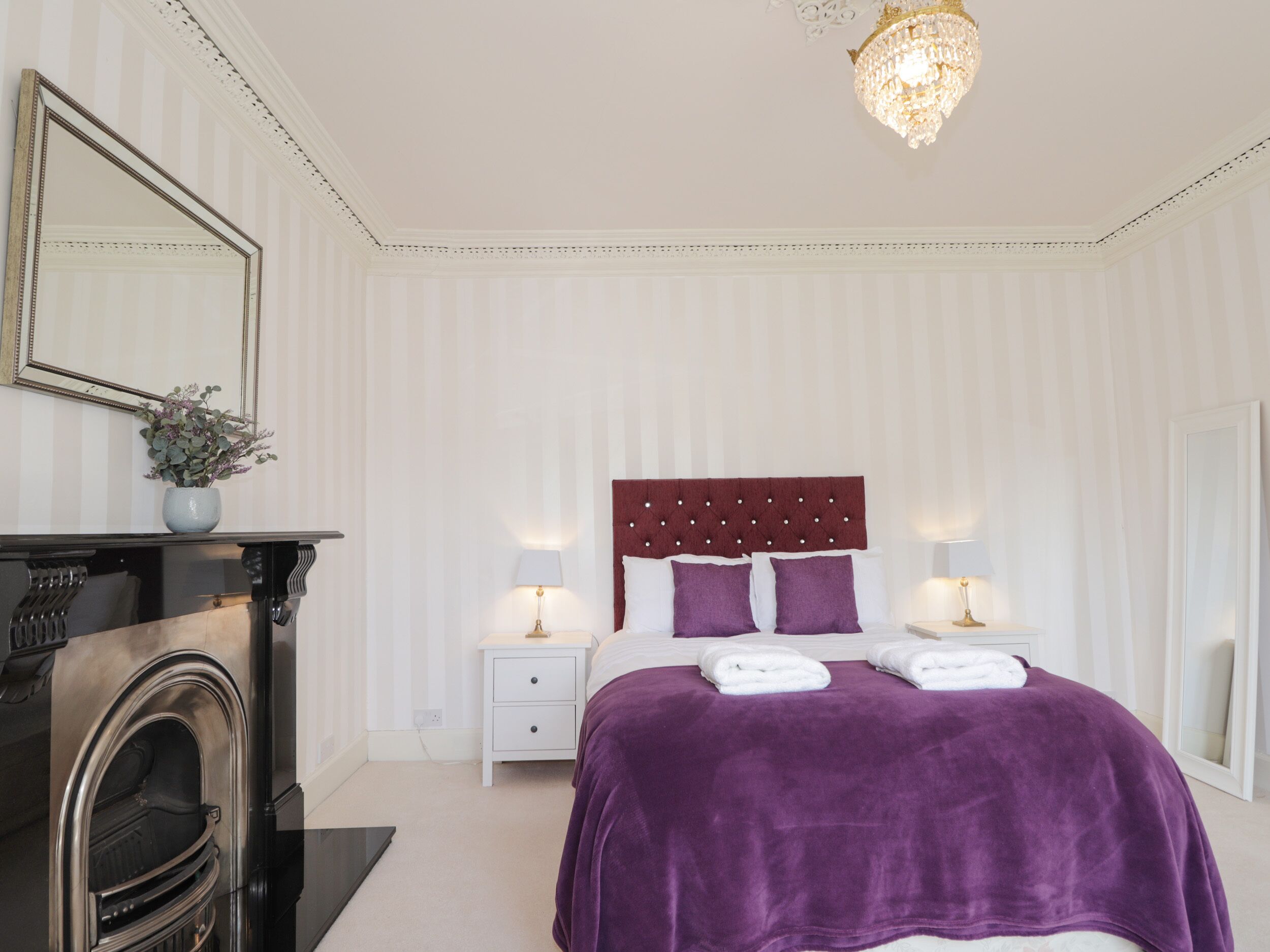 Een slaapkamer met een groot bed, twee nachtkastjes, een kaptafel, een spiegel en een kroonluchter.