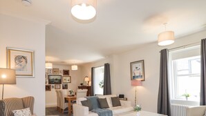 A well-lit living room with a sofa, armchair, coffee table, and dining area. - Mary Ann Villa (Inverness)