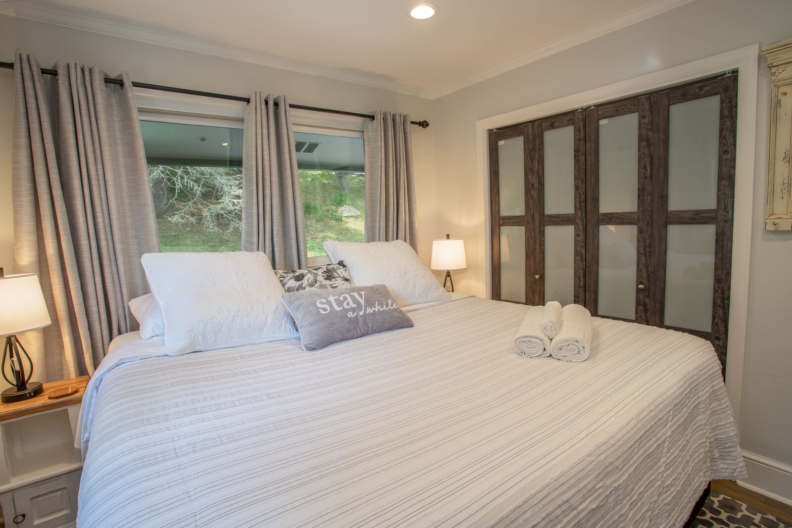 A neatly made bed with pillows, a bedside lamp, and a window with curtains.
