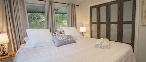 A neatly made bed with pillows, a bedside lamp, and a window with curtains.