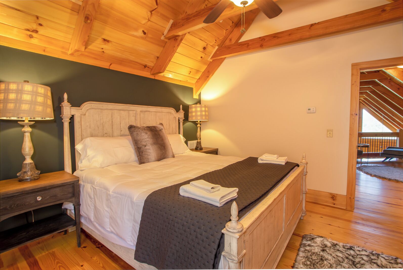 A bedroom with a wooden ceiling, a bed with white bedding, a grey blanket, and two bedside lamps.