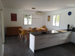 Uma cozinha moderna com uma ilha central, uma mesa de jantar com cadeiras amarelas e um armário de madeira.