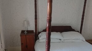 A four-poster bed with a wooden frame and white bedding, a nightstand with a lamp, and a patterned rug on a wooden floor. - Old Classic House in Suburbs  (Bulawayo)