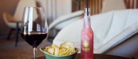 Habitación de hotel con una mesa de comedor que presenta una copa de vino tinto, un tazón de papas fritas y una botella de refresco de toronja rosa.