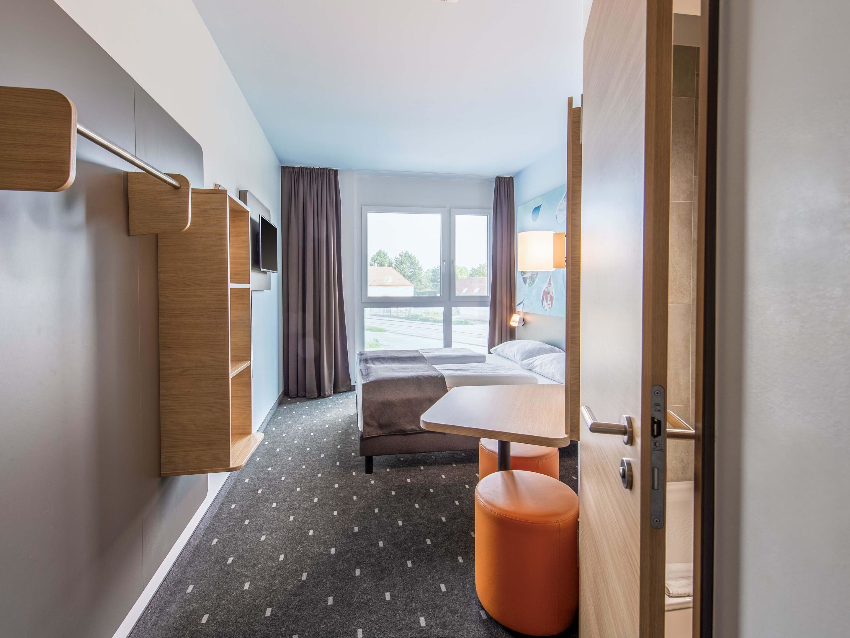 A hotel room with a bed, a desk, a chair, a TV, and a window with a view of the outside.