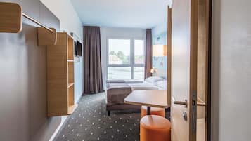 A hotel room with a bed, a desk, a chair, a TV, and a window with a view of the outside.