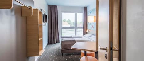 Habitación de hotel con cama, escritorio, silla, televisor y ventana con vistas al exterior.
