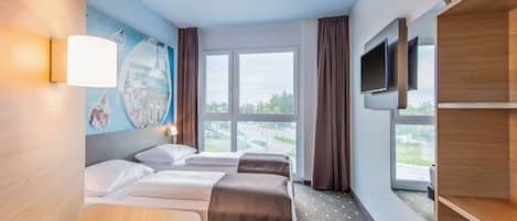 Quarto de hotel com duas camas, uma escrivaninha, televisão e uma janela grande com vista para a cidade.